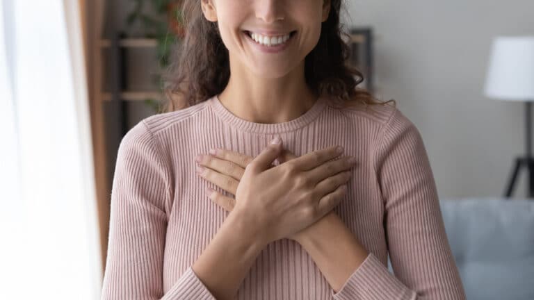 Close up of happy sincere woman folding her hands over her chest showing gratitude